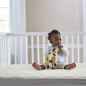 Infant sitting on the crib with the Quilted crib mattress pad