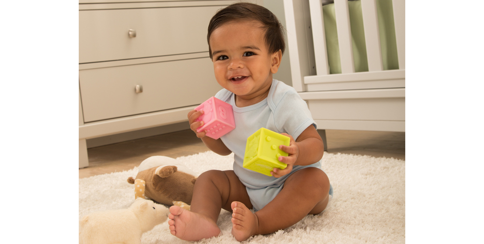 Smiling baby sitting on a rug playing with toys.