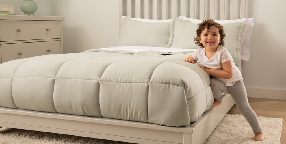 Toddler leaning on the edge of a bed smiling.