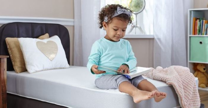 Toddler sitting on a toddler bed and reading