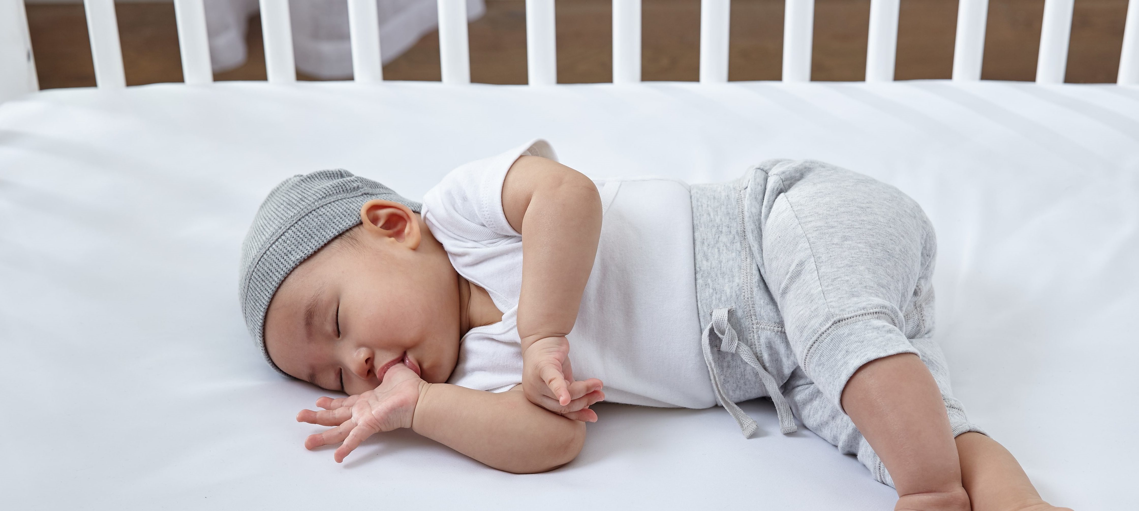 infant sleeping on Sealy crib mattress while sucking his thumb